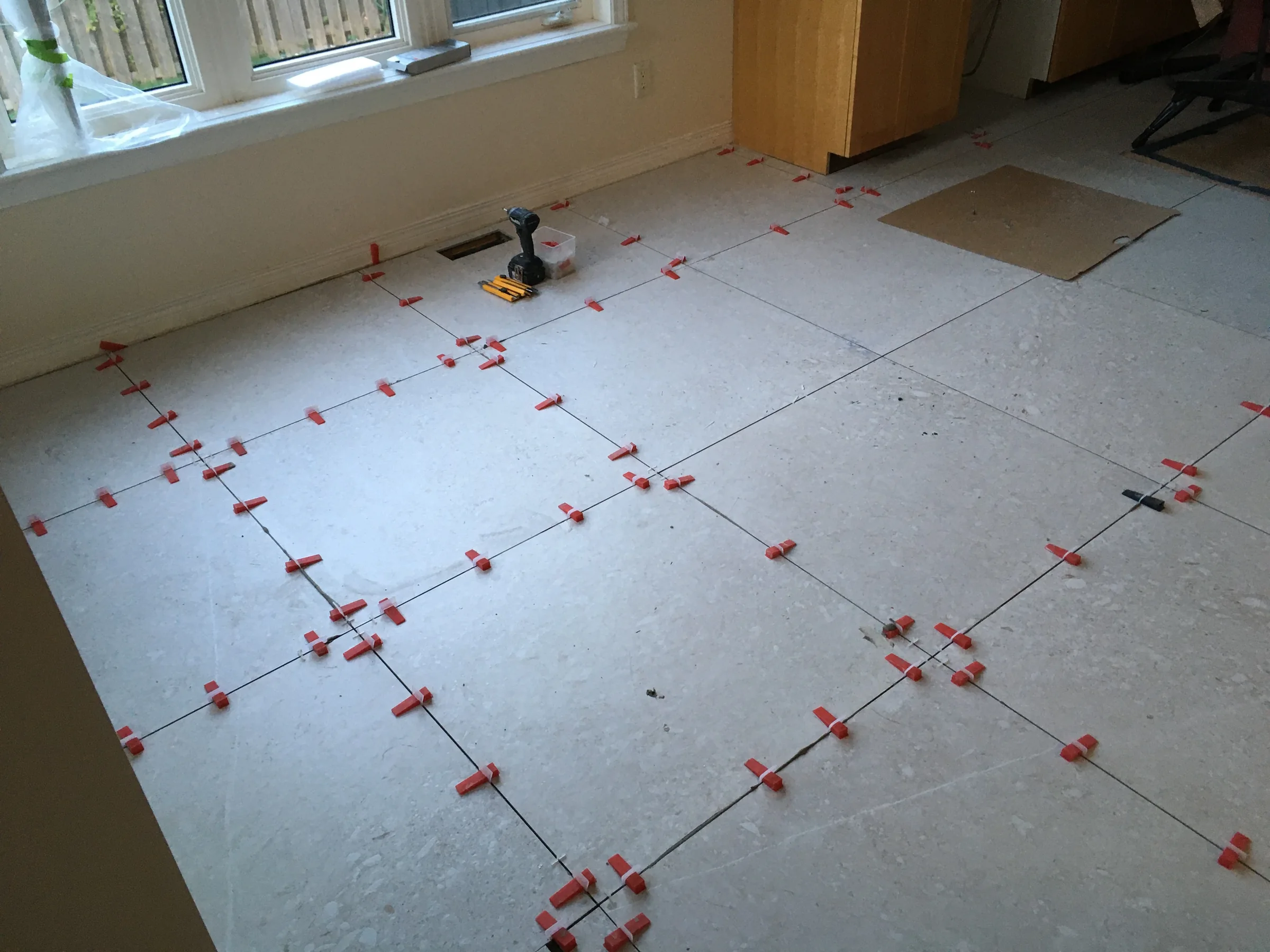 Large-format floor tile installation in progress with levelling clips and a planned layout